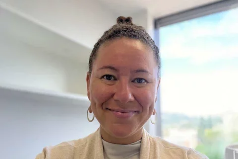 Woman with earrings and cream colored top in front of window