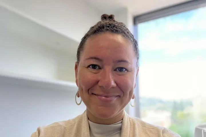 Woman with earrings and cream colored top in front of window
