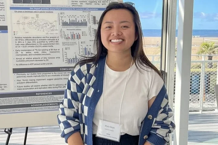 woman in white shirt, blue checkered sweater, standing in front of a scientific poster
