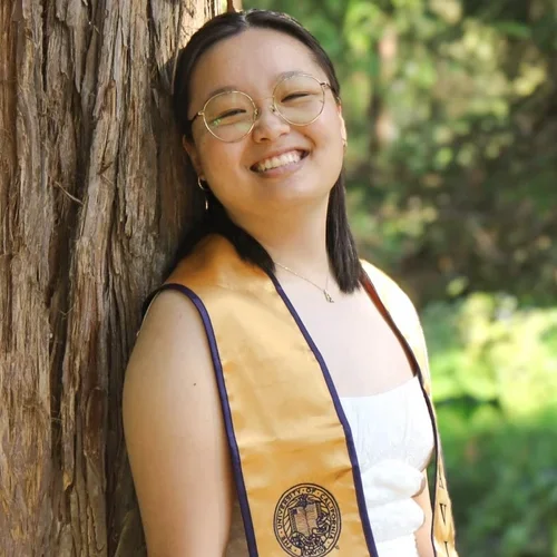 woman leaning against tree wearing graduation sash