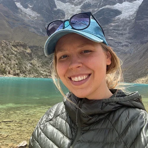 female with hat on standing in front of lake and mountain