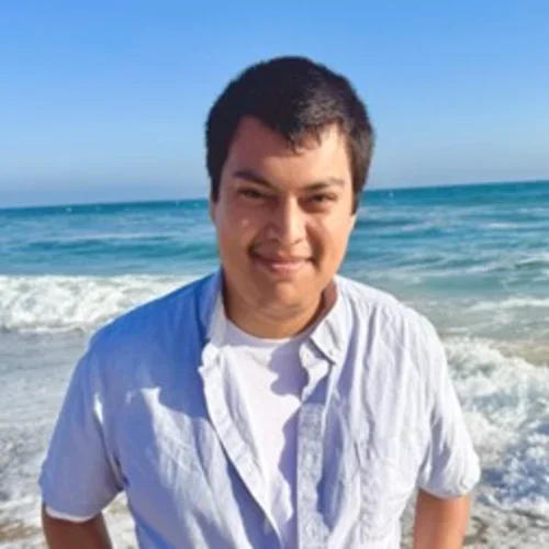 male in light blue shirt in front of ocean