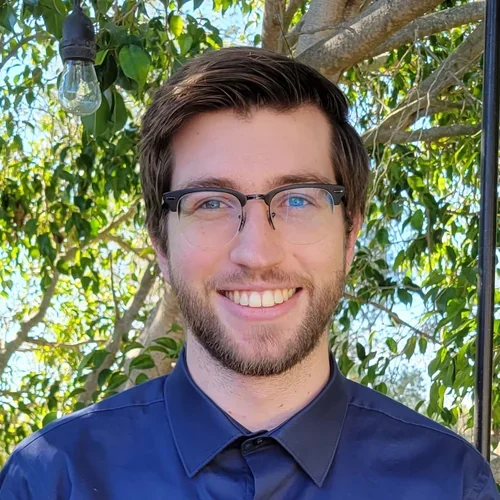 male in blue shirt and glasses smiling at camera