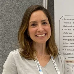 woman with dark shoulder length hair and a light top next to a poster