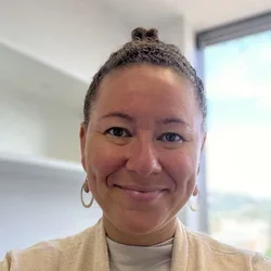 Woman with earrings and cream colored top in front of window