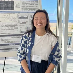 woman in white shirt, blue checkered sweater, standing in front of a scientific poster