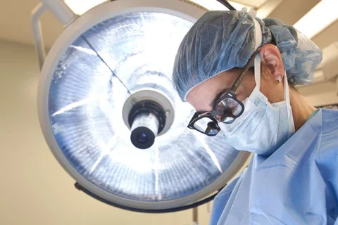 Photo of Doctor in surgery with surgical lamp behind them